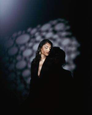 Artistic portrait with moody lighting and bokeh background showing a figure in black against dark shadows.