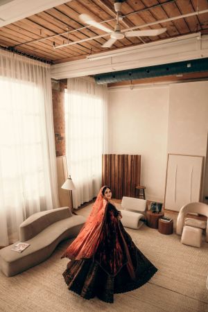 Dramatic twirling shot of a black and red lehenga in an industrial-style room with wooden beams.