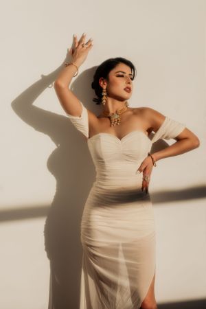 Dramatic fashion portrait in cream dress with strong shadow play against white background.