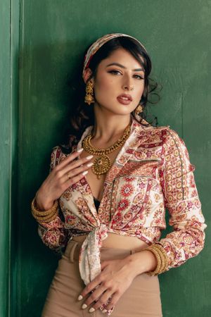 Fashion portrait showcasing traditional Indian jewelry and paisley print blouse against emerald wall.