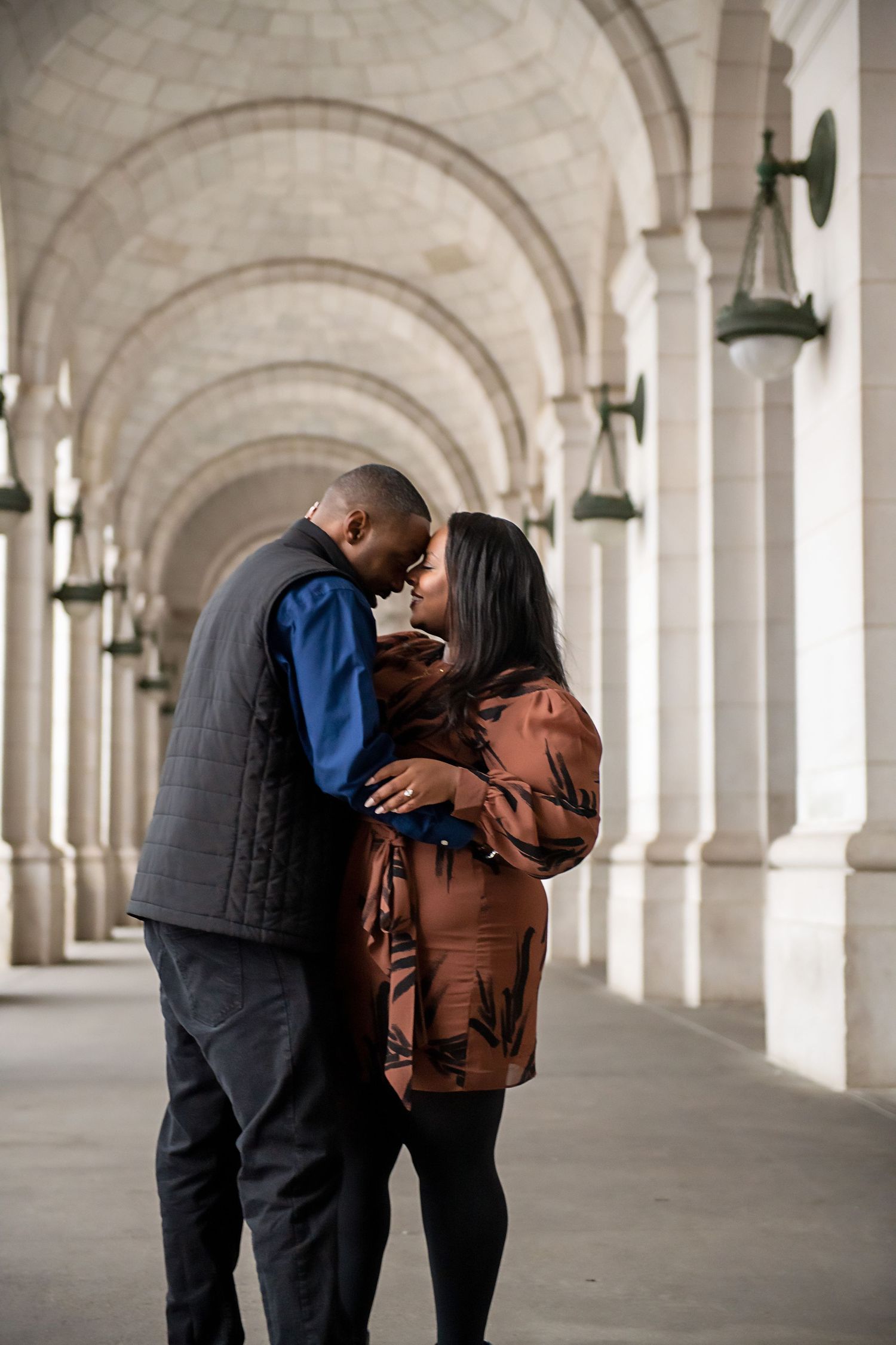 Romantic couple embracing in arched hallway with classical architecture.