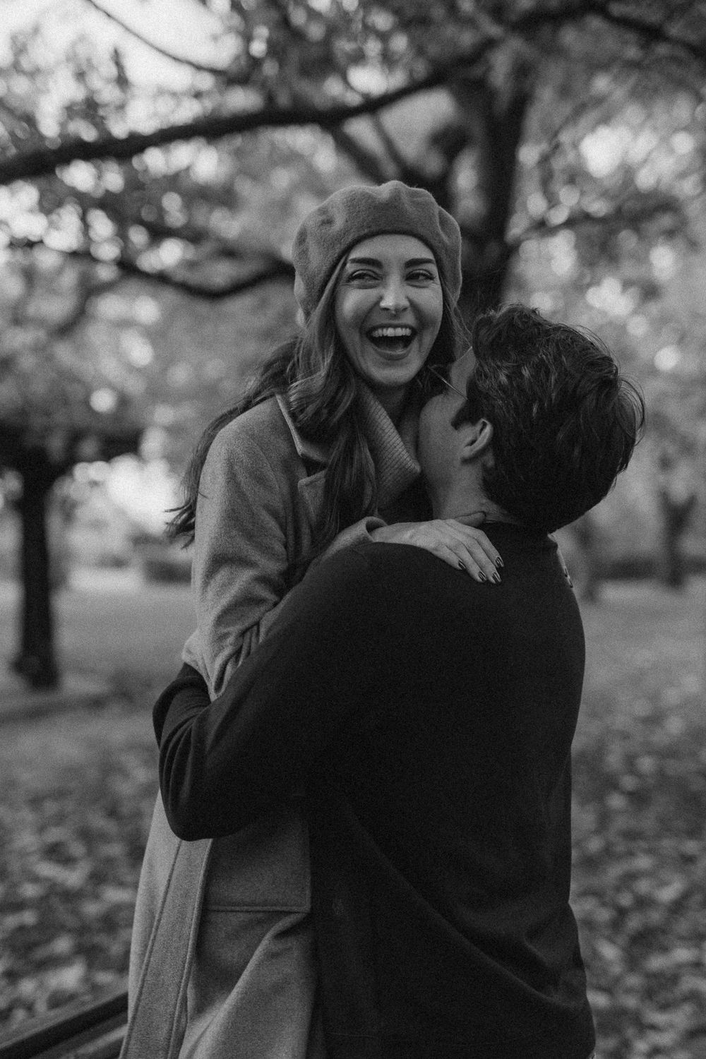 Joyful couple sharing a romantic moment outdoors among autumn trees in black and white.