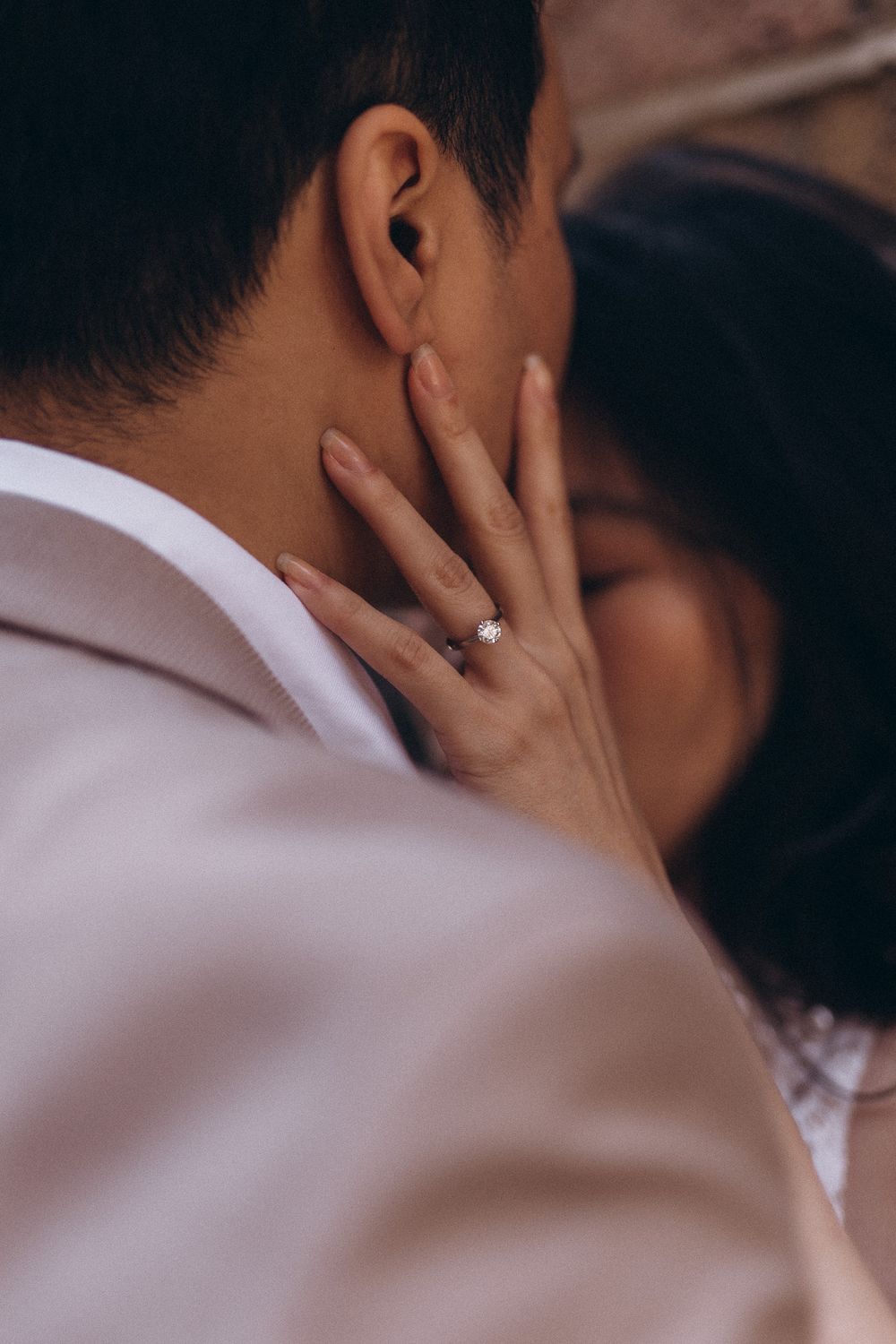 Close-up of a delicate hand with an engagement ring touching a person's neck in a romantic moment.