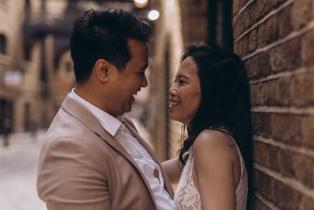 Happy couple laughing together against a brick wall in warm natural lighting.