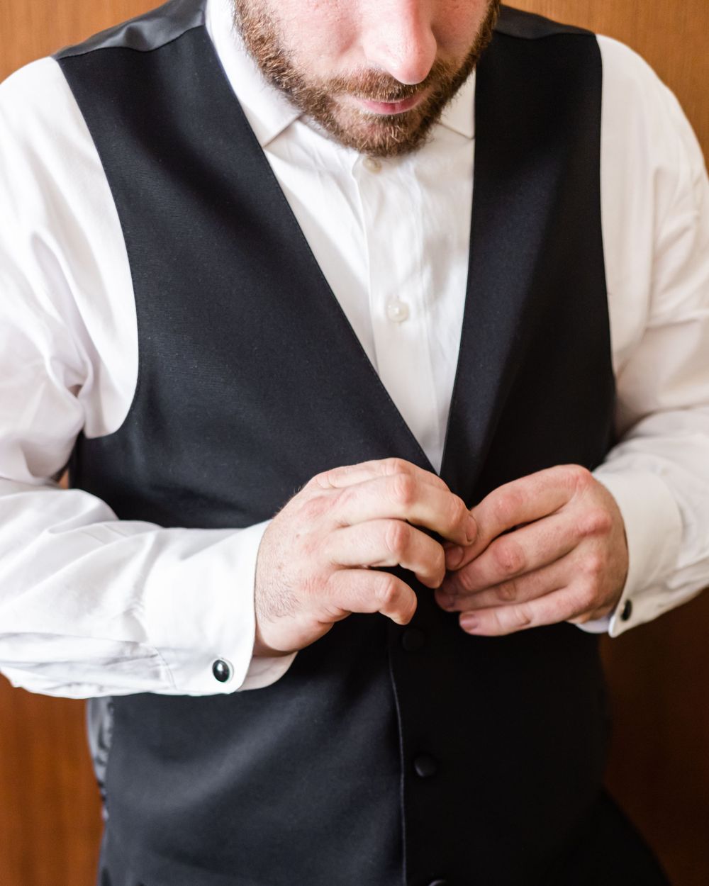 Close-up of formal black vest and white dress shirt being buttoned.