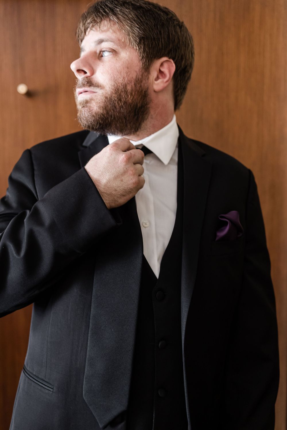 Person in formal black suit adjusting tie with purple pocket square.