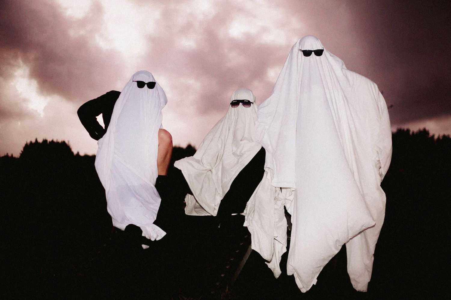 Ghostly figures in white sheets move mysteriously under pink cloudy skies.