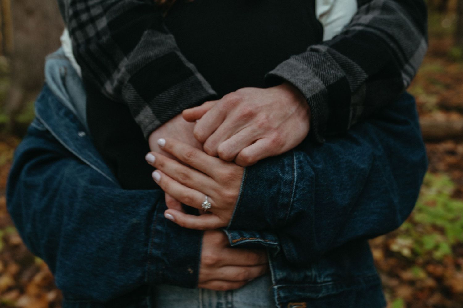 Close-up of clasped hands wearing denim and plaid in autumn setting.