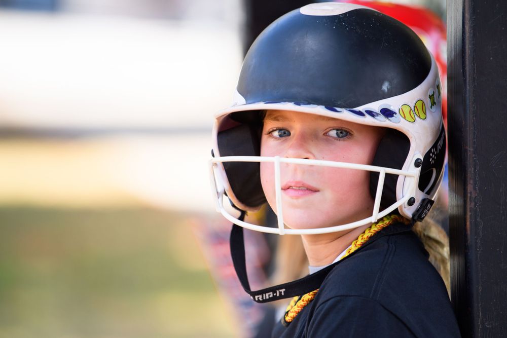 Player in batting helmet looking from dugout during softball game.