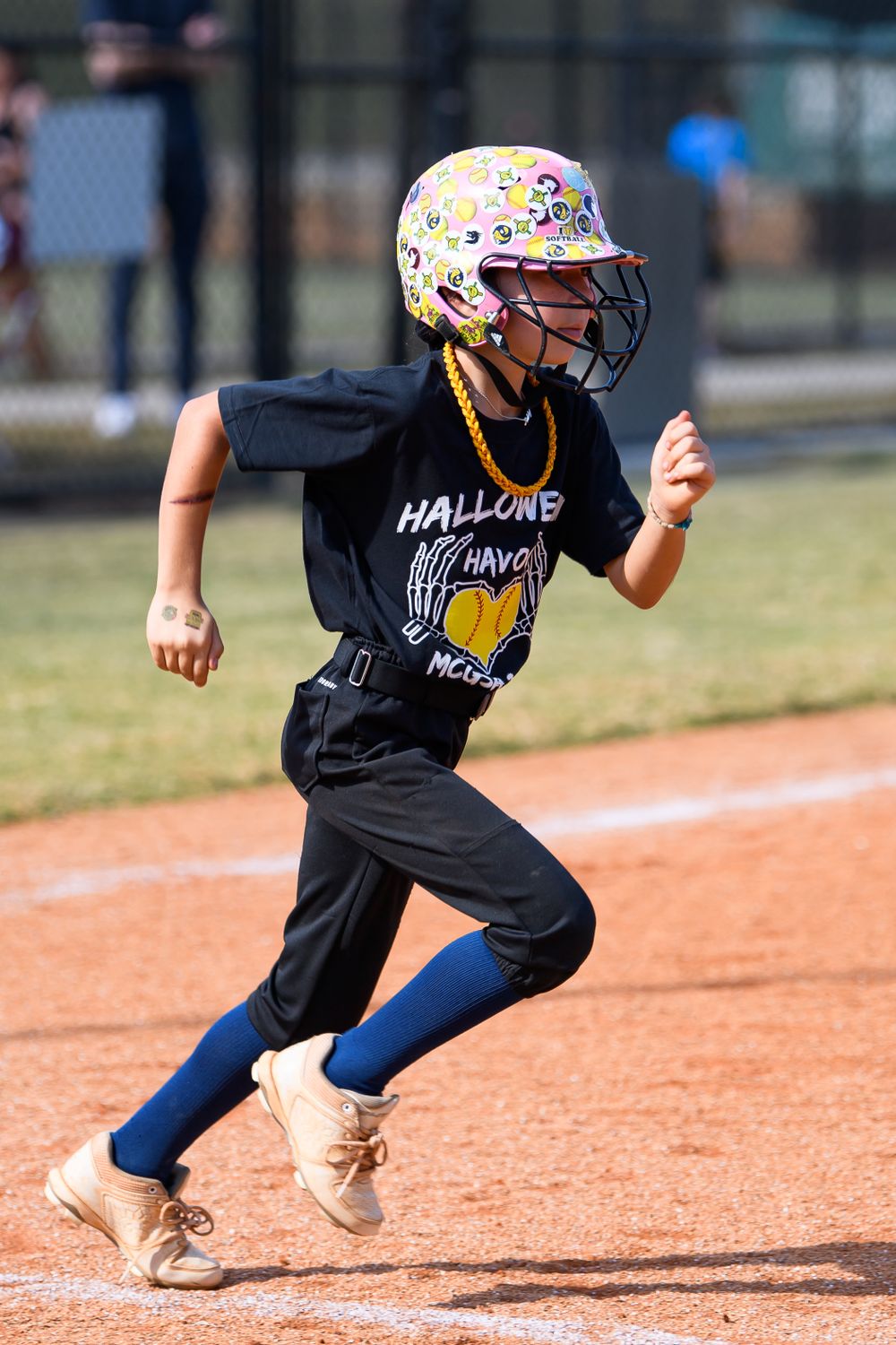Young player in decorated helmet running on baseball diamond wearing team uniform.