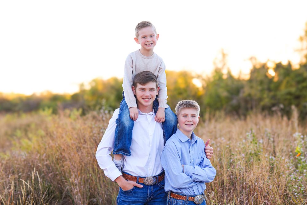 Three people pose together in a sun-lit field during golden hour.