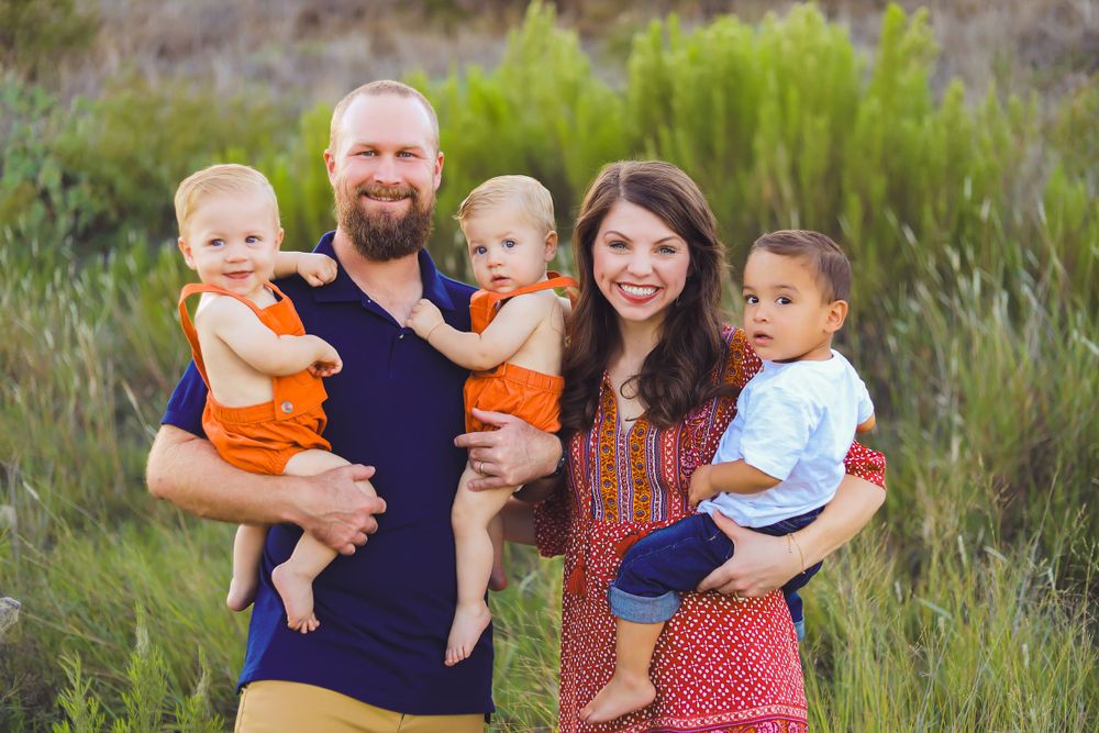 A family group portrait in a natural outdoor setting with tall grass and foliage in the background.