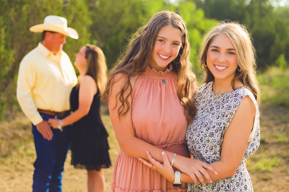 Two women in summer dresses pose together while others stand in background during sunset.