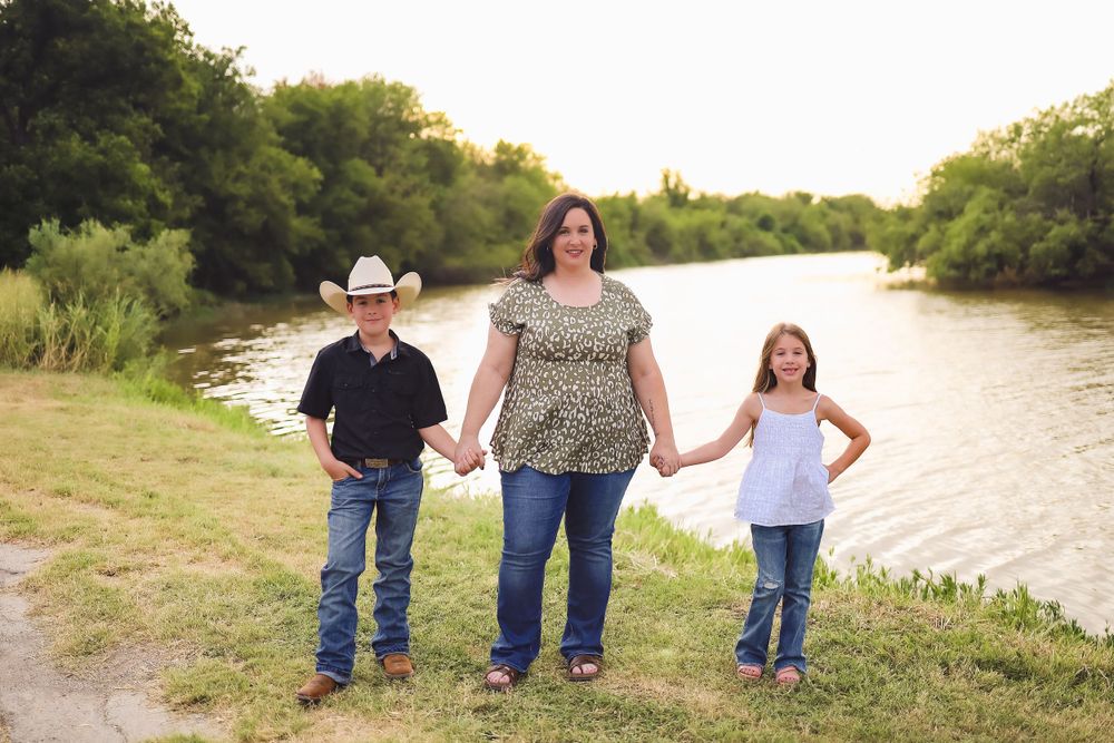 Three people standing together by a serene river during sunset.