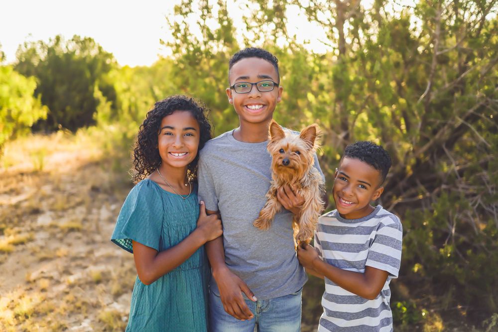 Children posing with their adorable small dog outdoors on a sunny afternoon.
