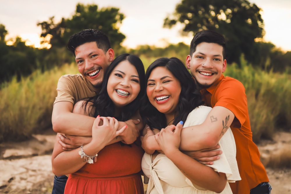 Four people embracing and laughing together during outdoor sunset photo session.