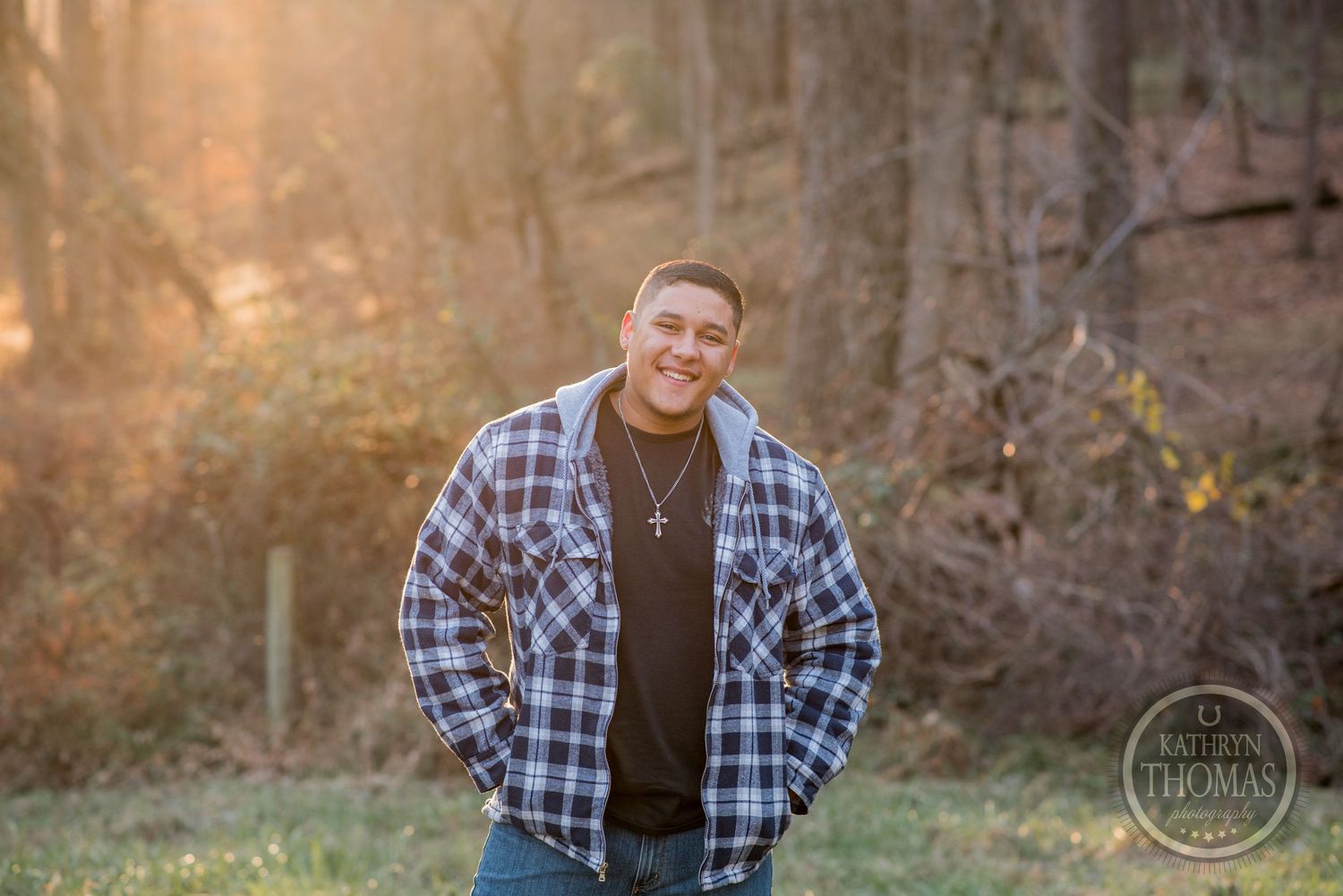 A person in plaid flannel and jeans poses with a warm smile against an autumn forest backdrop.