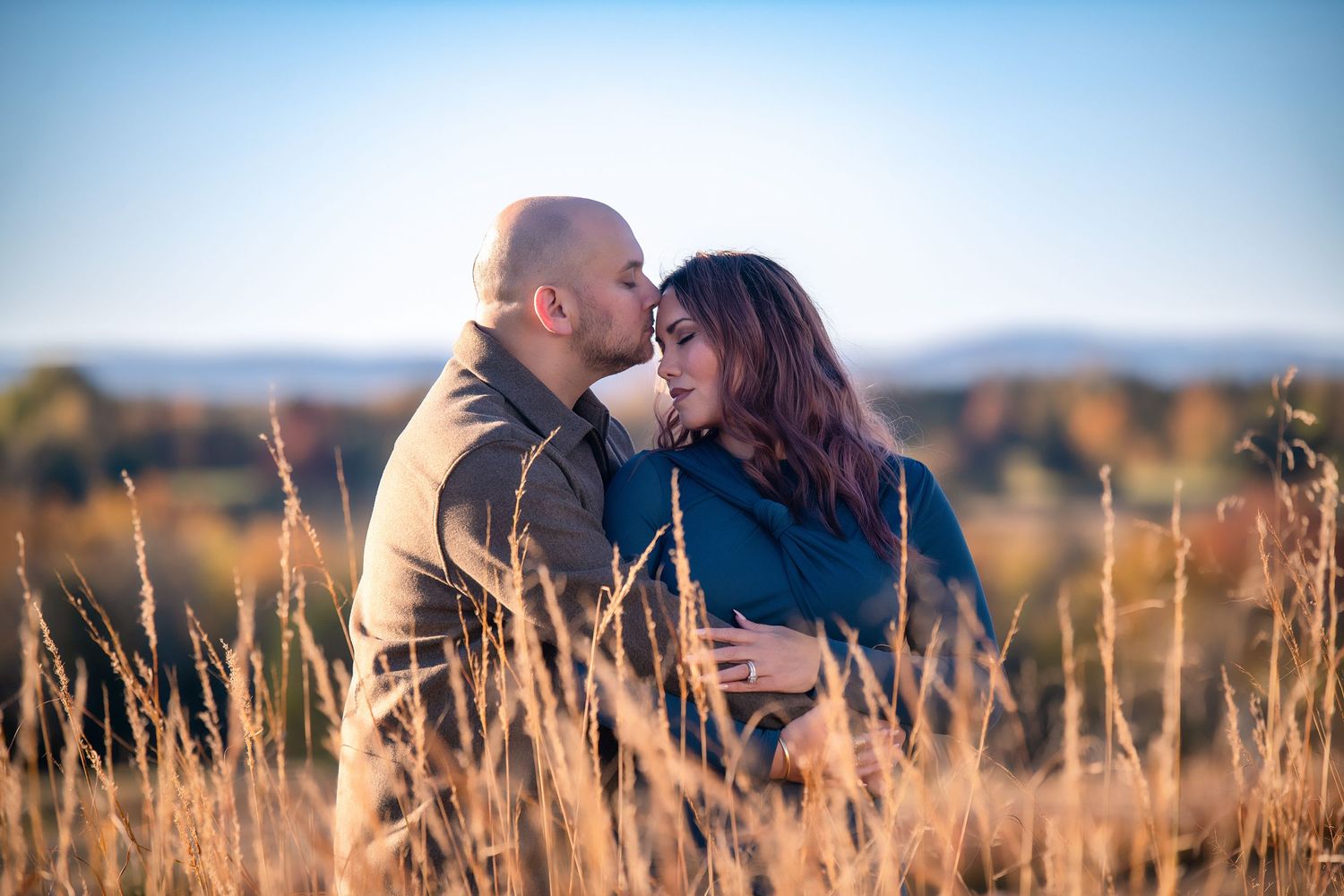 A romantic couple shares a tender moment among tall grass during sunset.