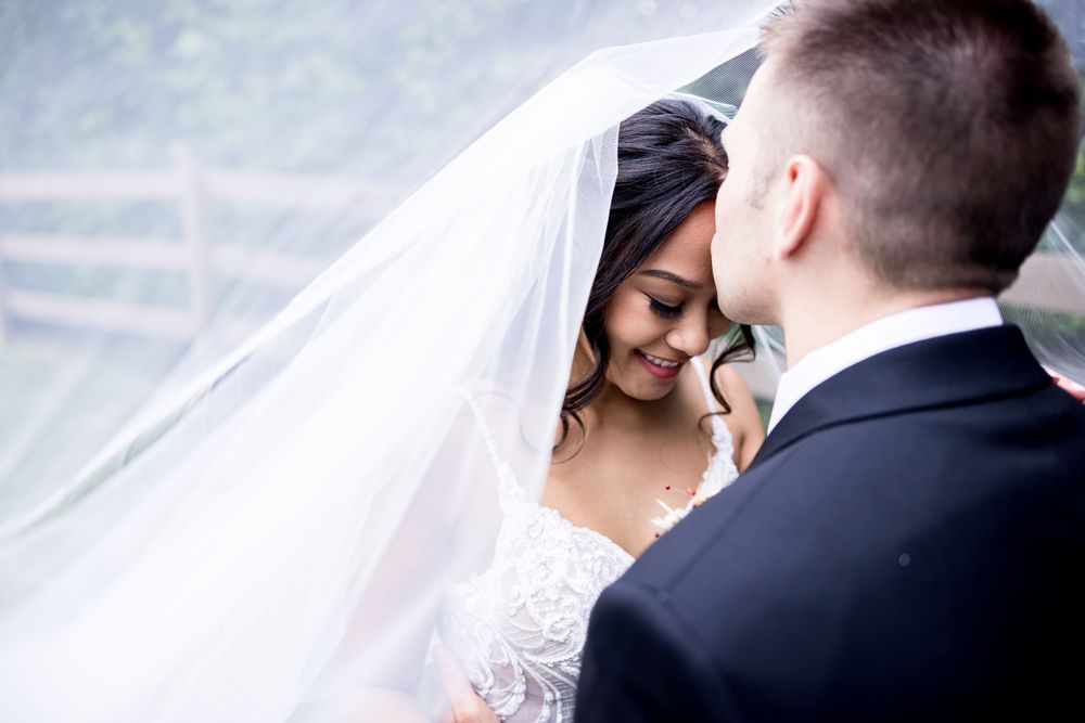 A romantic wedding moment captured under a flowing white veil as newlyweds share an intimate embrace.