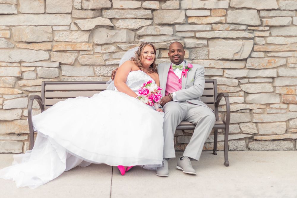 A bride and groom share a tender moment together on a bench against a stone wall background at their wedding.
