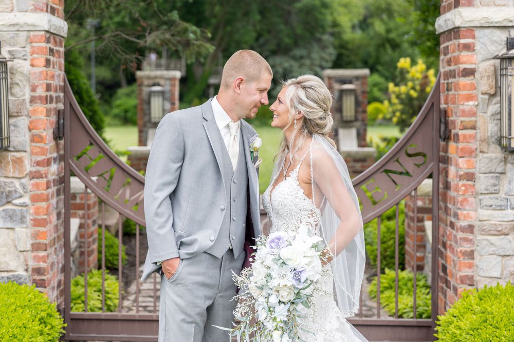 A couple shares a romantic moment in front of ornate brick garden gates while dressed in wedding attire.