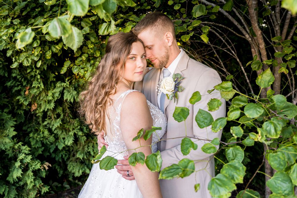 A romantic wedding couple embraces in a lush garden setting with green ivy and natural lighting.