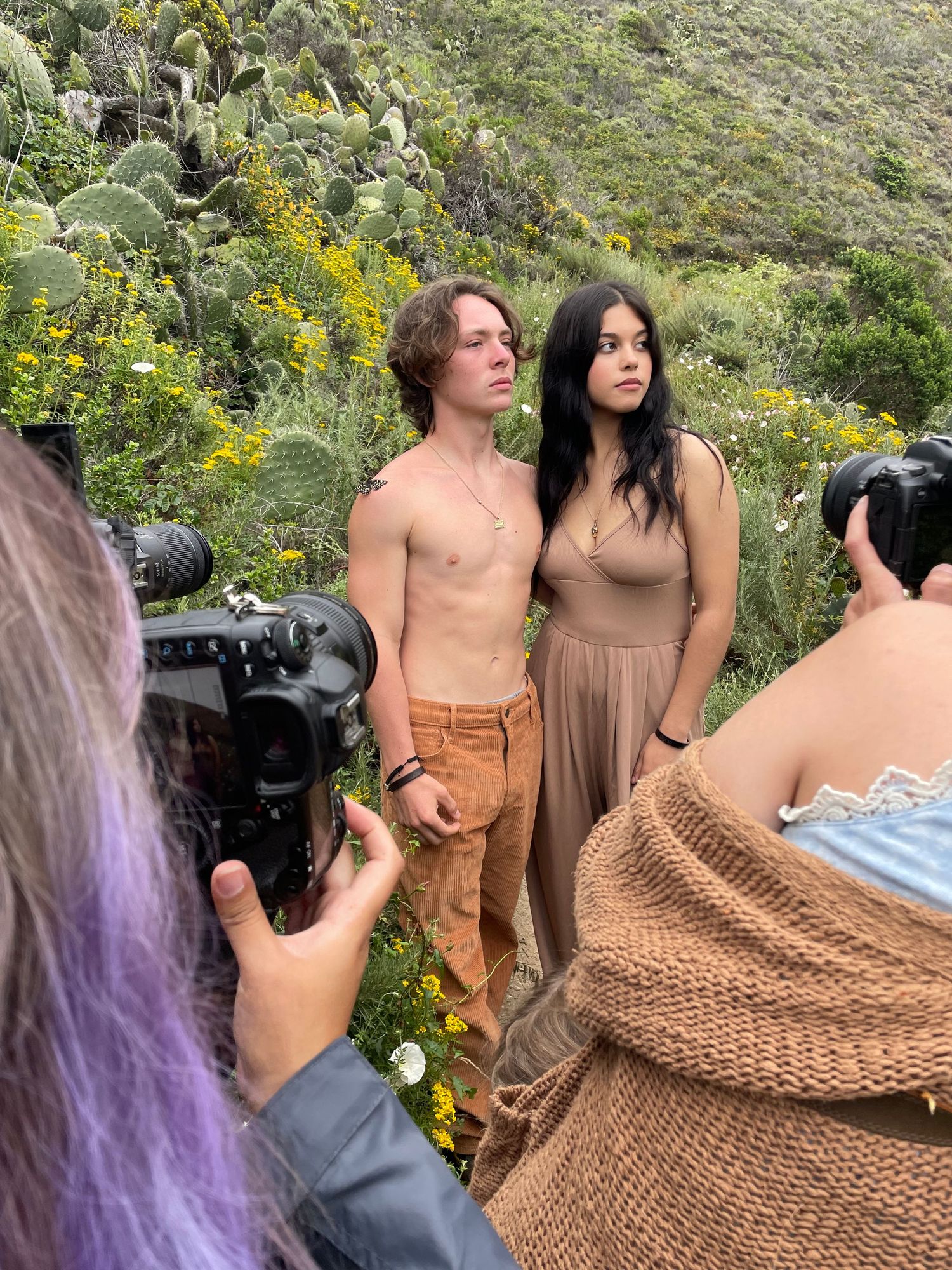 Behind-the-scenes photoshoot with models and photographers in a field of yellow wildflowers and cacti.
