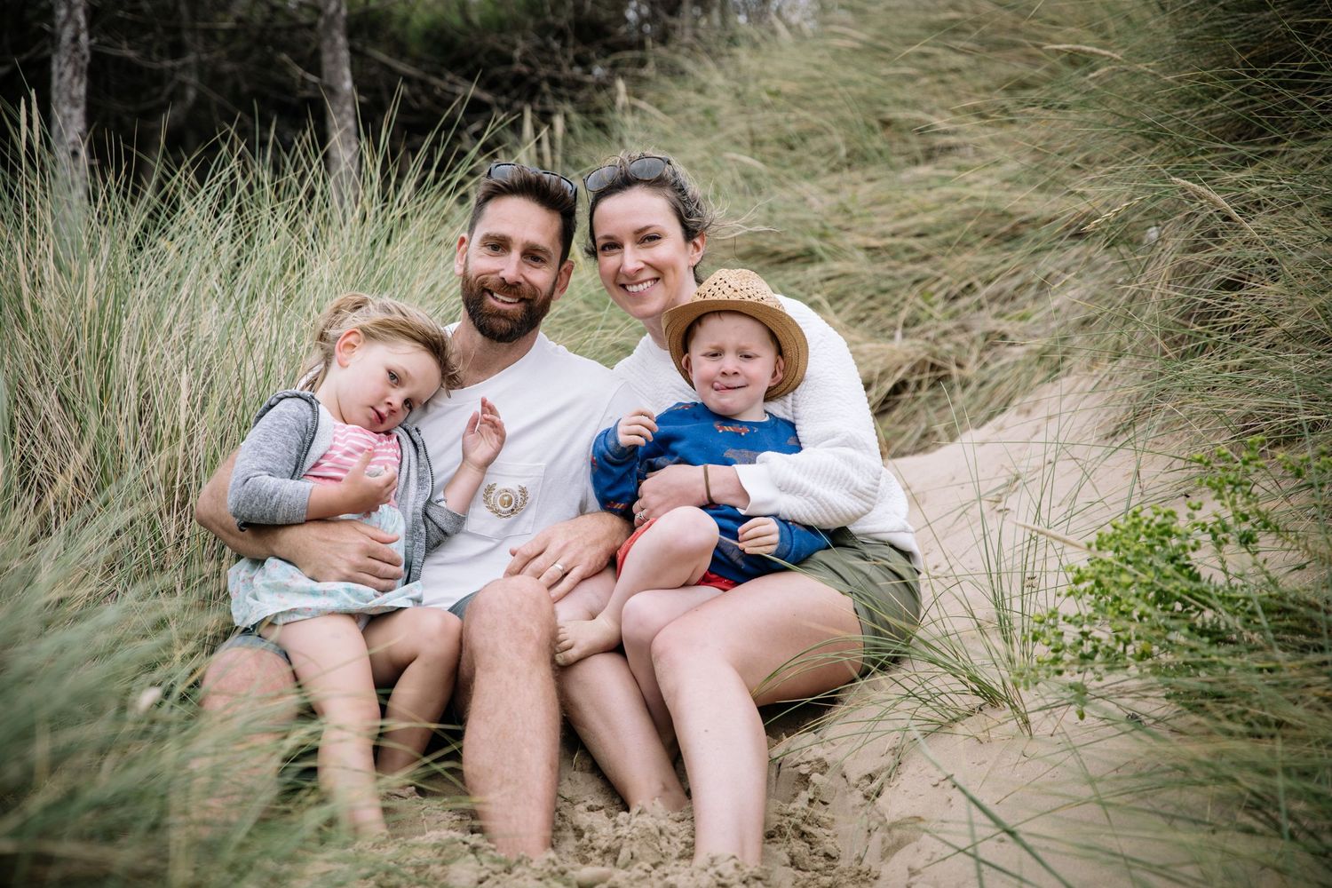 A family sitting together on sandy dunes surrounded by tall beach grass.