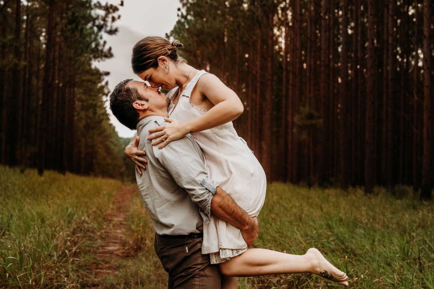A romantic embrace between a couple in a wooded forest clearing at sunset.