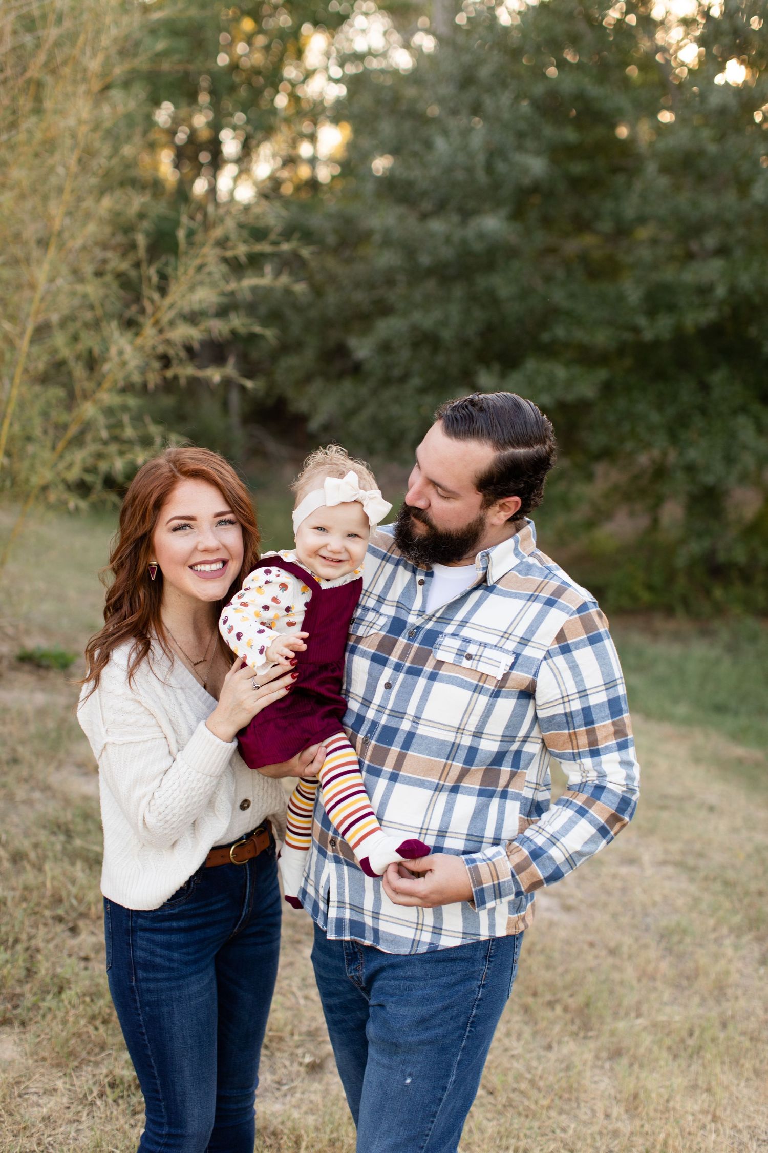 Family of three sharing tender moment outdoors in casual attire.