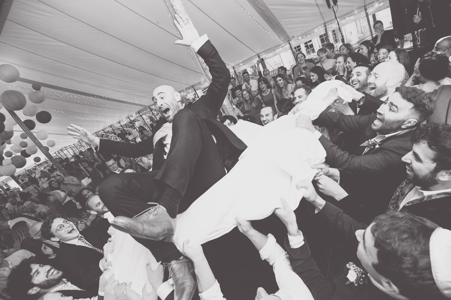 Crowd surfing celebration at lively wedding reception under tent.