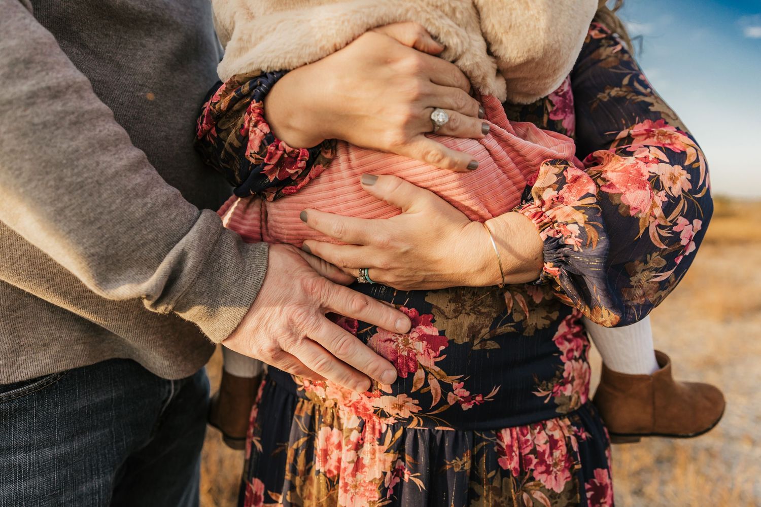 Series of hands cradling a pregnant belly wearing a floral dress.