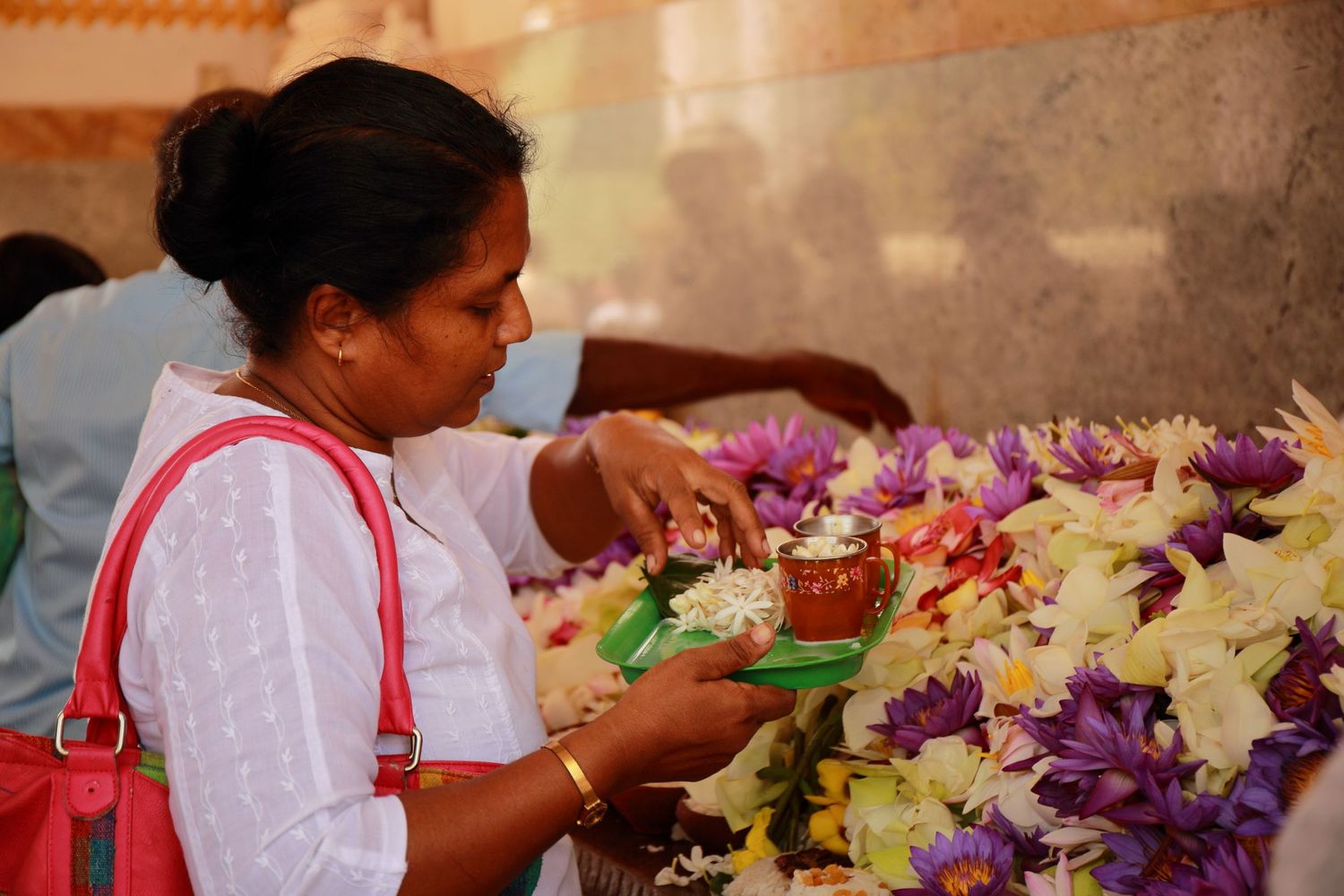 Woman in white arranging colorful flowers and offerings at a Buddhist temple ceremony.