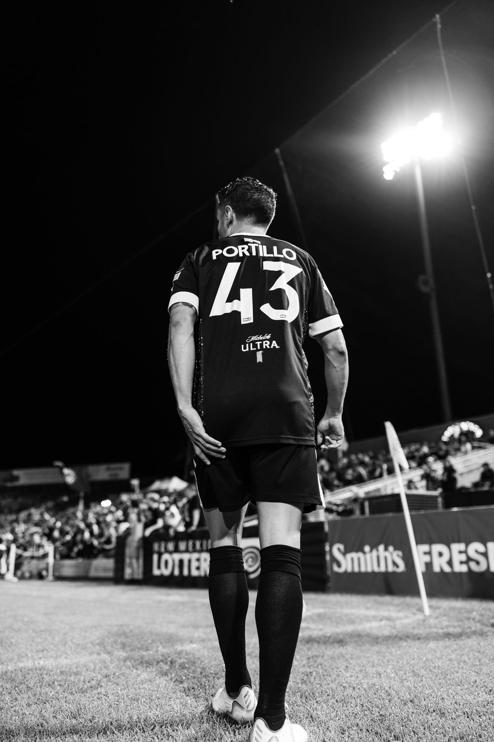 Soccer player wearing jersey number 43 stands under stadium lights in black and white photo.