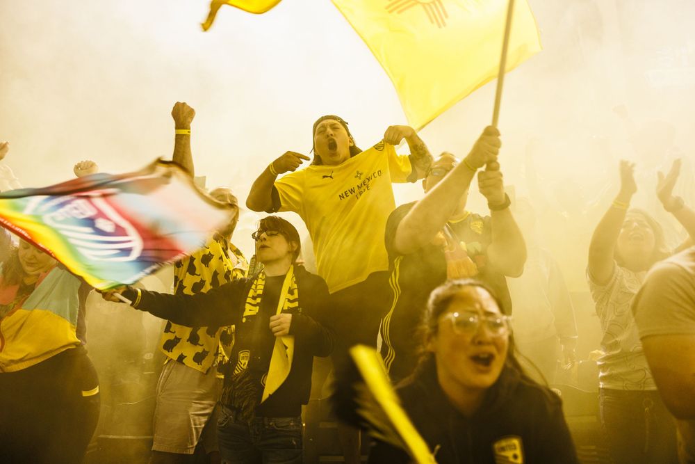 Passionate soccer fans cheering with yellow flags and smoke in the crowd.