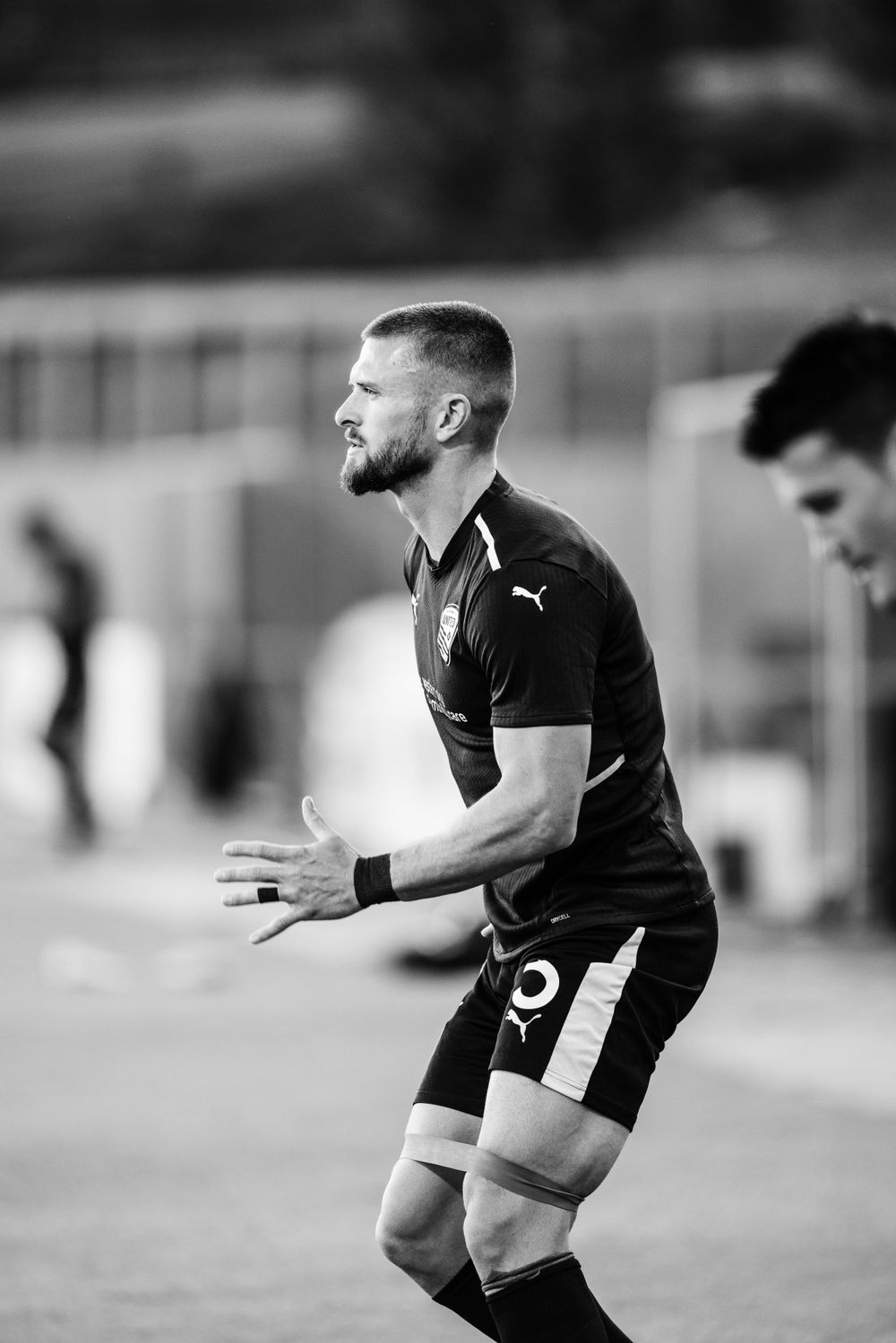 Soccer player in black uniform gestures during match in monochrome image.