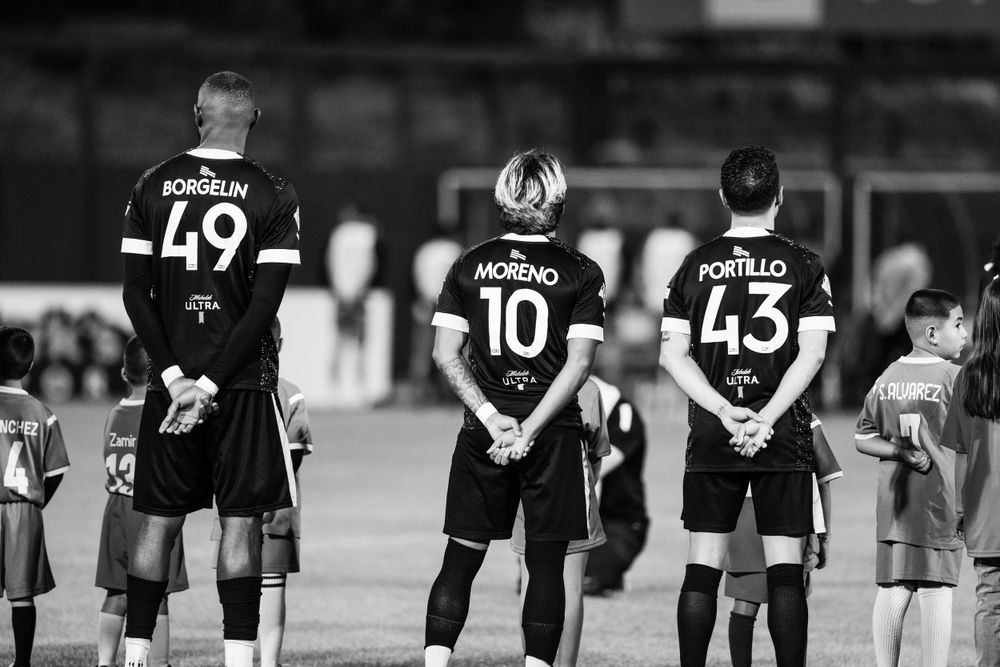 Soccer players lined up with jersey numbers 49, 10, and 43 during nighttime match.