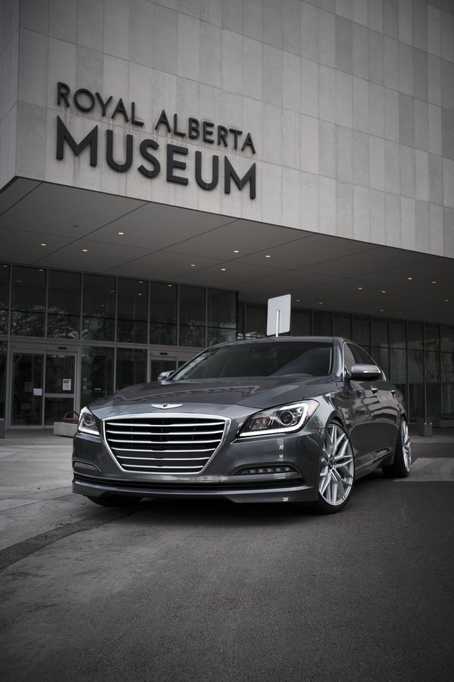 Grey luxury car displayed in front of Royal Alberta Museum entrance.
