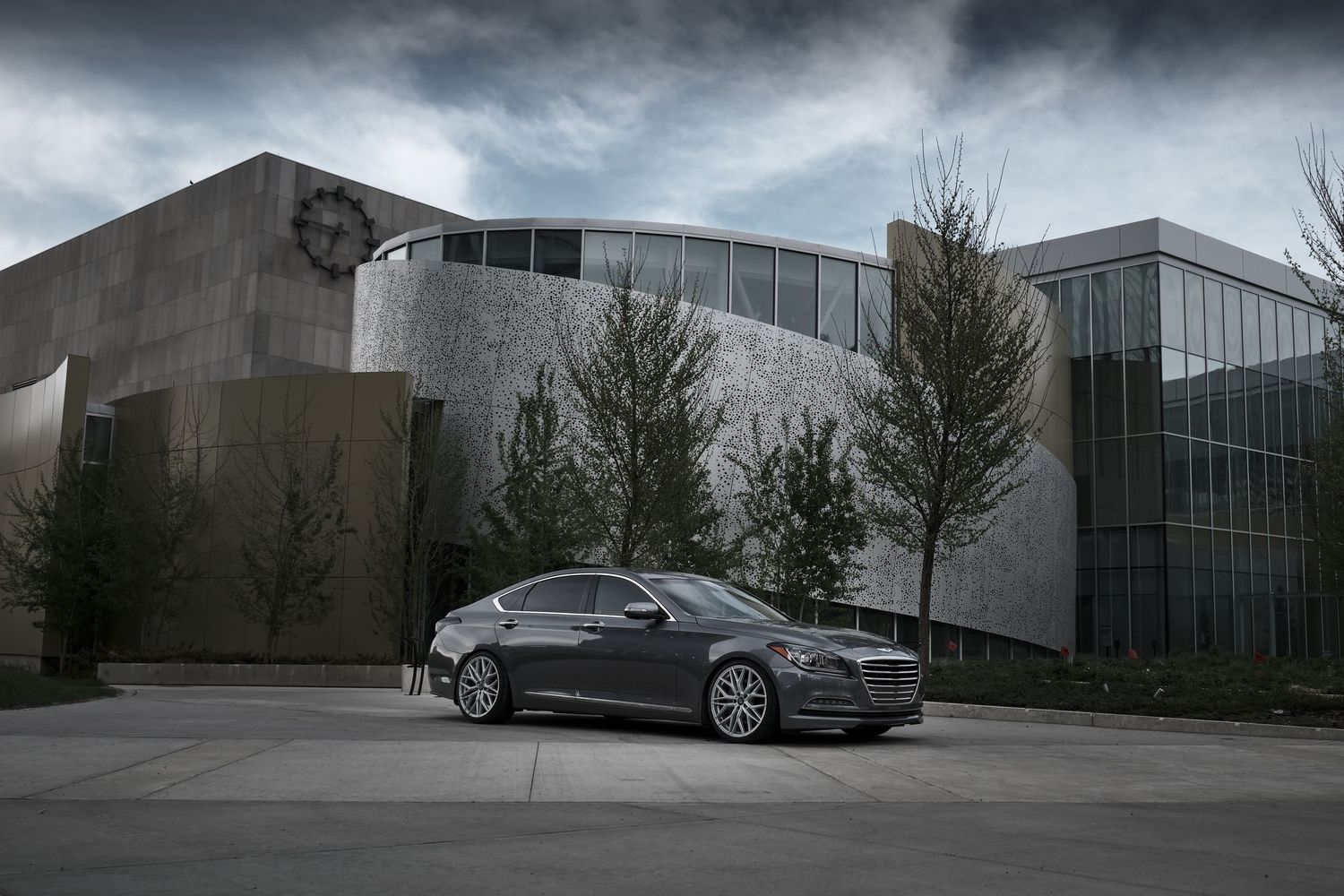 Luxury sedan parked outside modern architectural building under dramatic cloudy sky.
