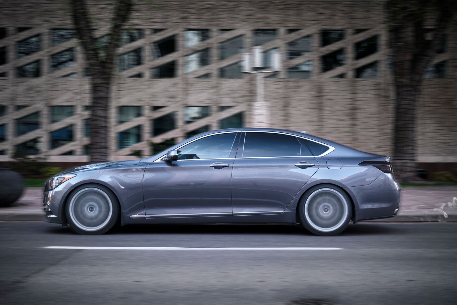 Profile view of grey luxury sedan in motion on city street.