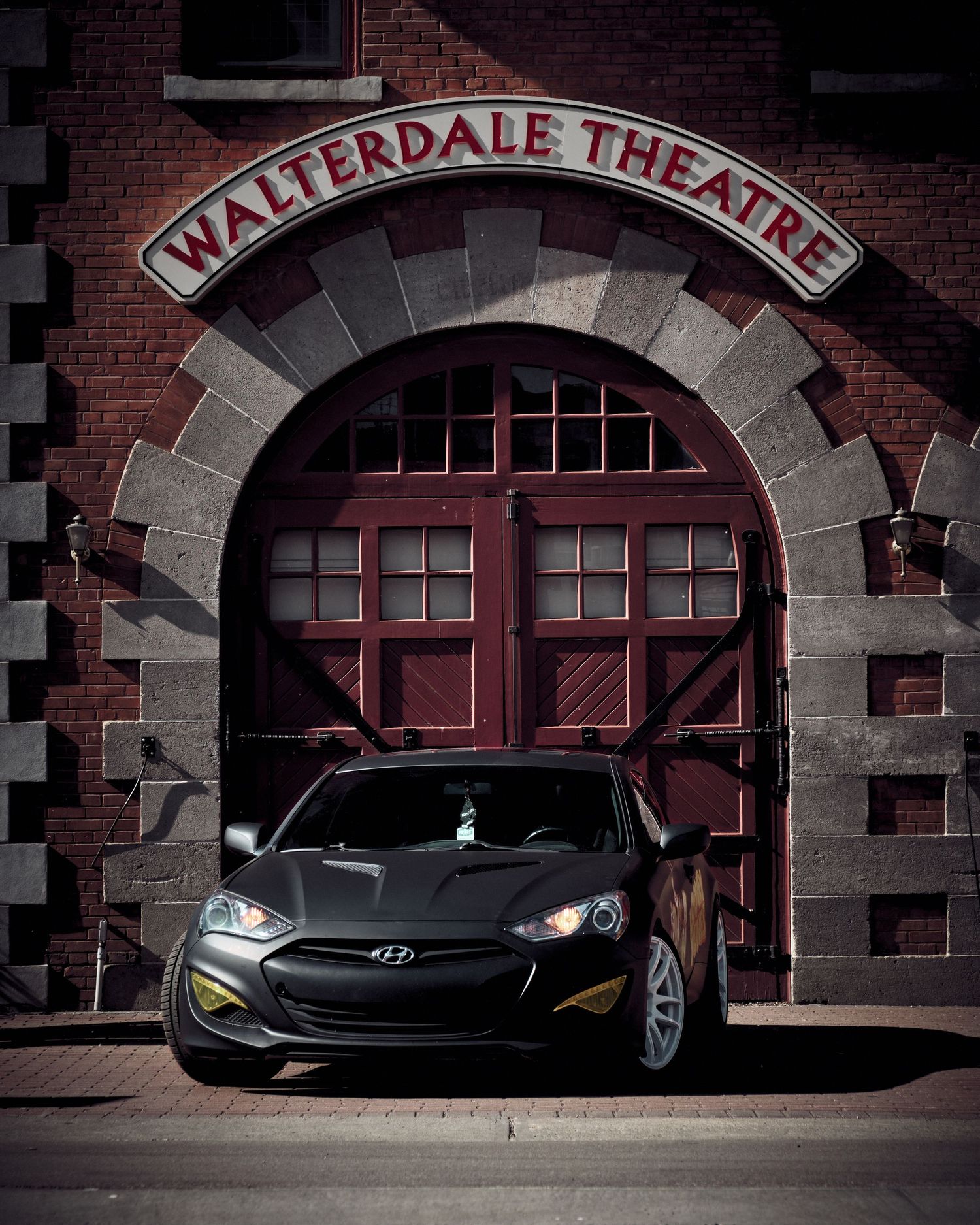 Hyundai Genesis coupe parked in front of historic Walterdale Theatre brick archway.