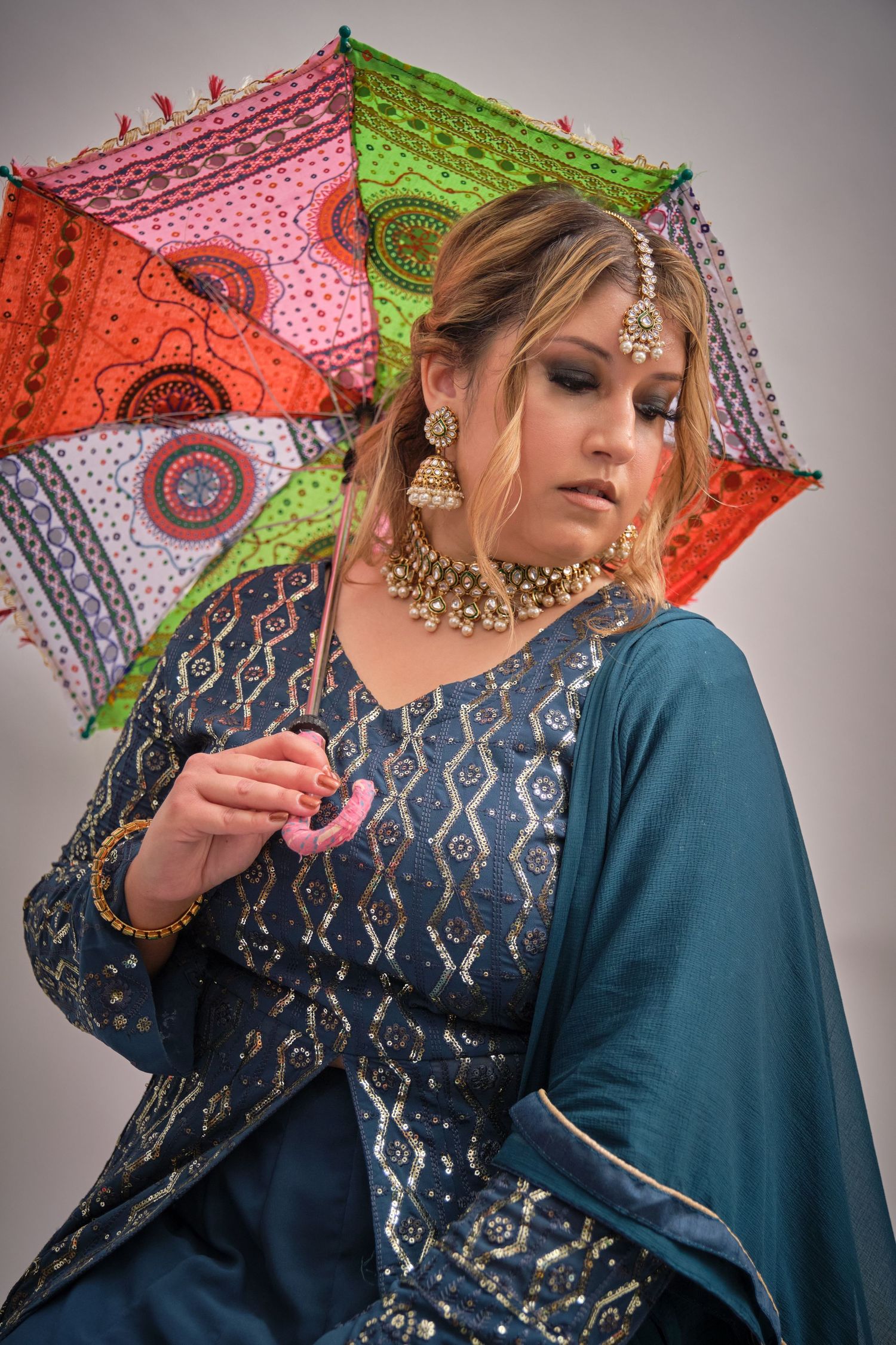 Traditional South Asian fashion with decorative parasol featuring vibrant patterns in red and green.