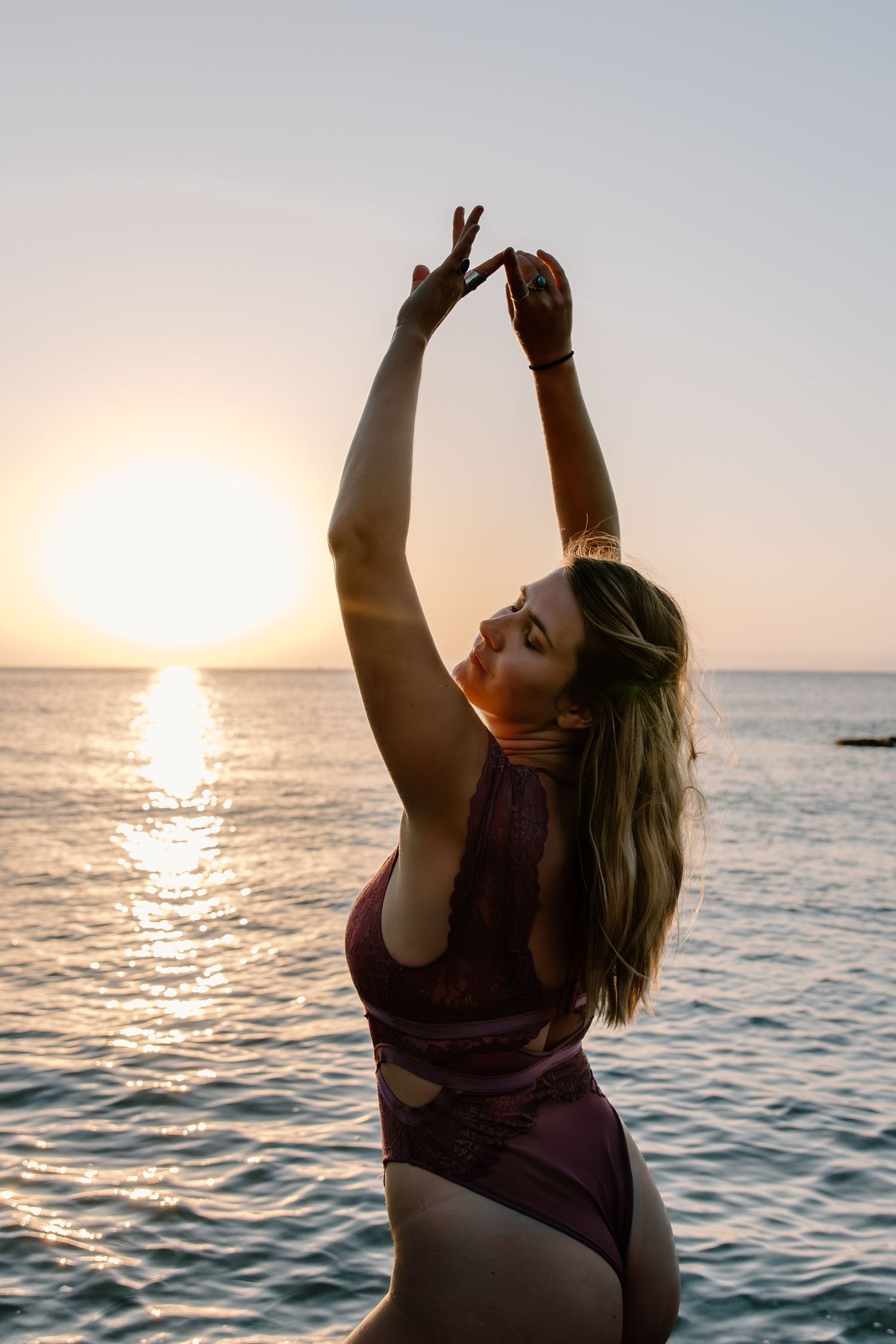 Joyful figure raises arms toward the setting sun over ocean waves.