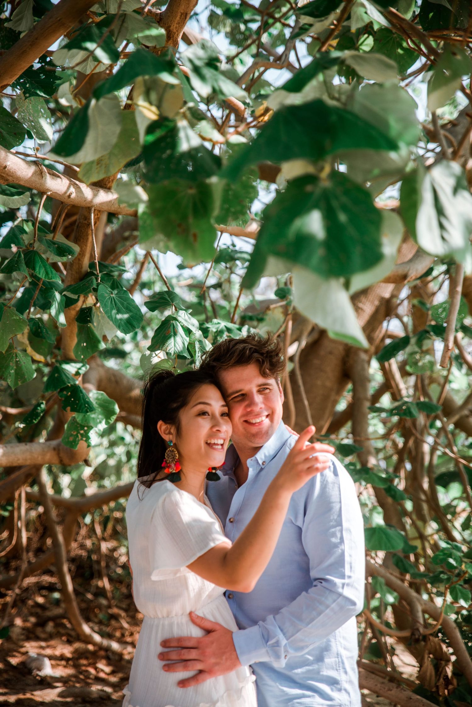 A couple shares a joyful moment among lush green foliage in natural lighting.