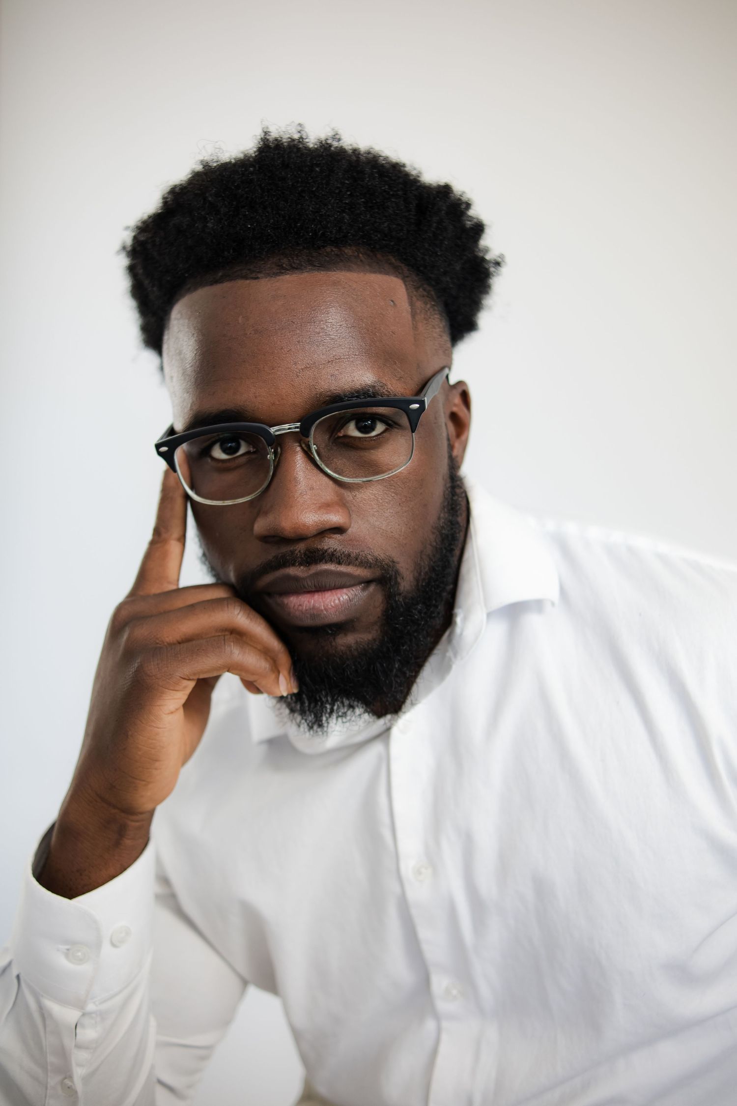 Professional portrait of person in glasses and white shirt with thoughtful expression against light background.
