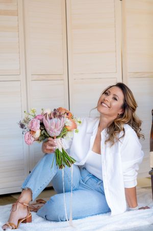 Casual lifestyle portrait featuring a floral bouquet with pink protea flowers and white ribbons.