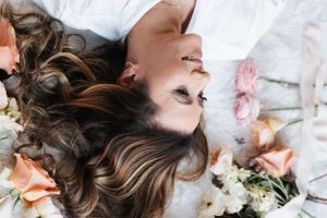 Dreamy overhead shot of someone lying among scattered flowers with peachy blooms.