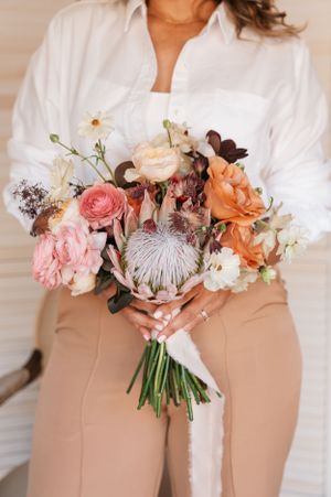 Close-up of beautiful floral bouquet with protea flowers and pink roses against neutral outfit.