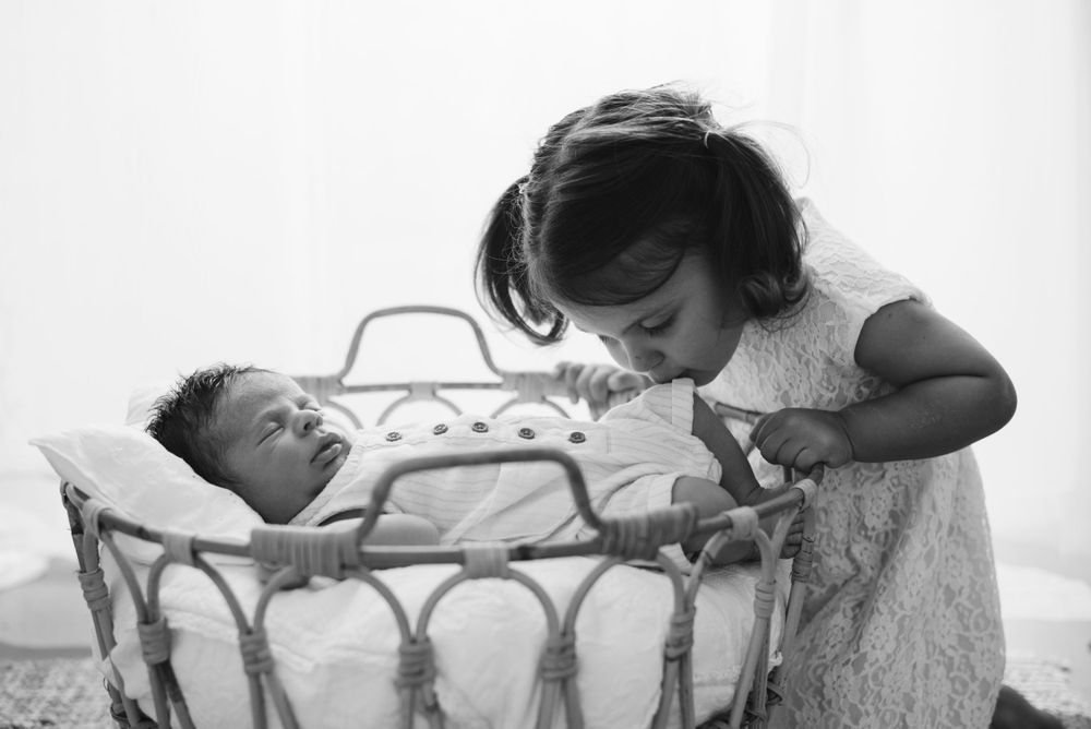 A tender moment captured in black and white as a child peers into a vintage baby bassinet.