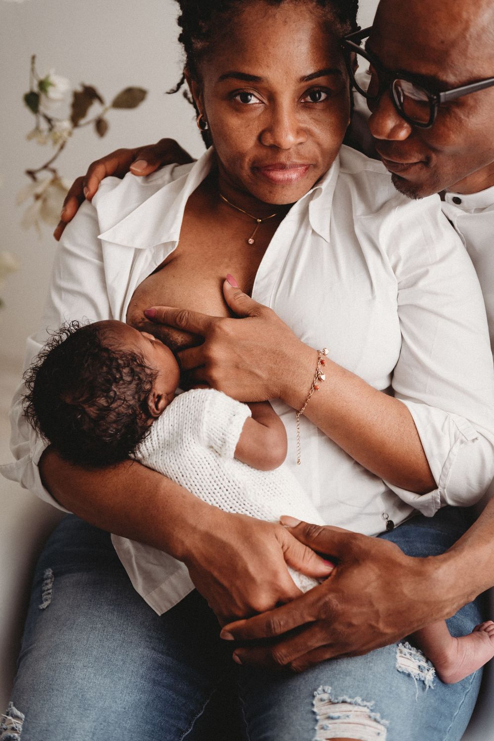 Parents lovingly embrace their newborn baby in white while sitting together.